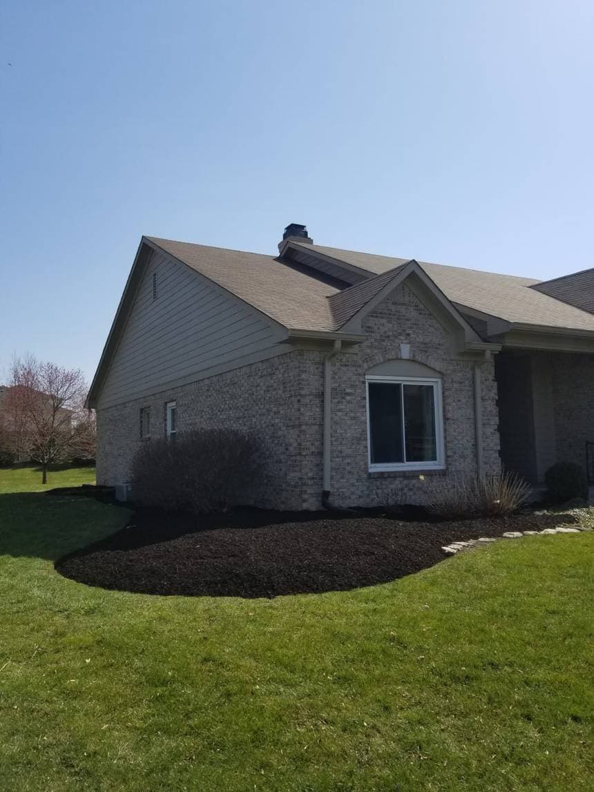 The corner of a brick house with a freshly mulched planting bed curving around it and cut lawn in front