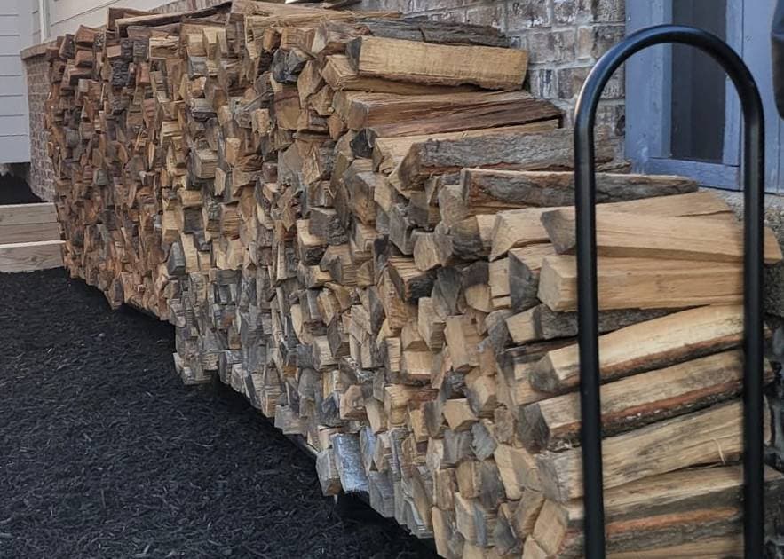 Split firewood stacked in a long row against a house wall